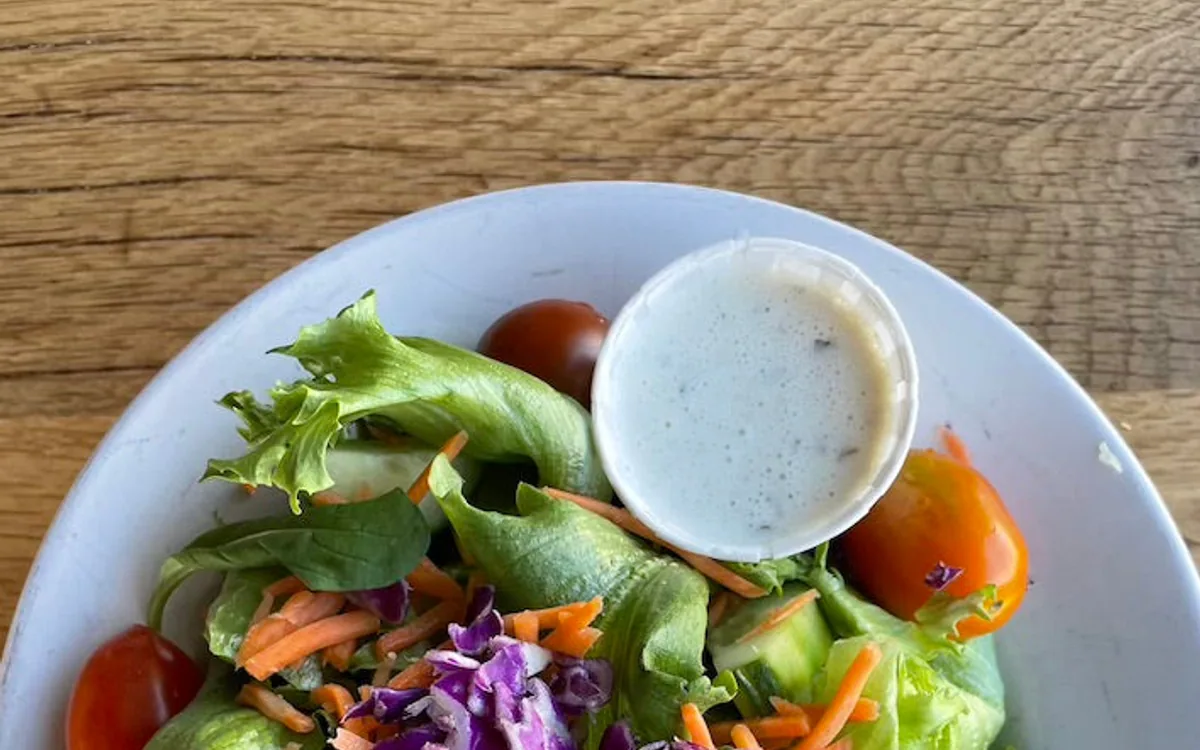 A bowl of salad with a side of dressing