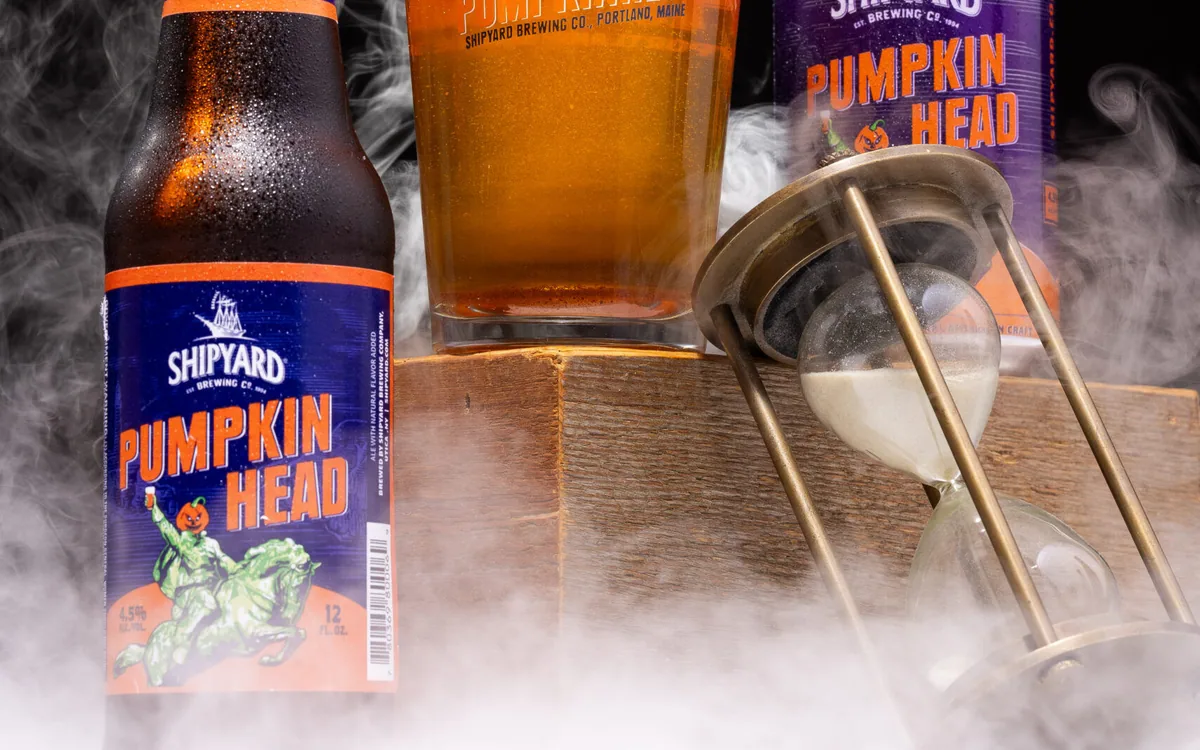 Bottle and glass of Shipyard Pumpkin Head beer on a wooden surface with a dark background and smoky fog