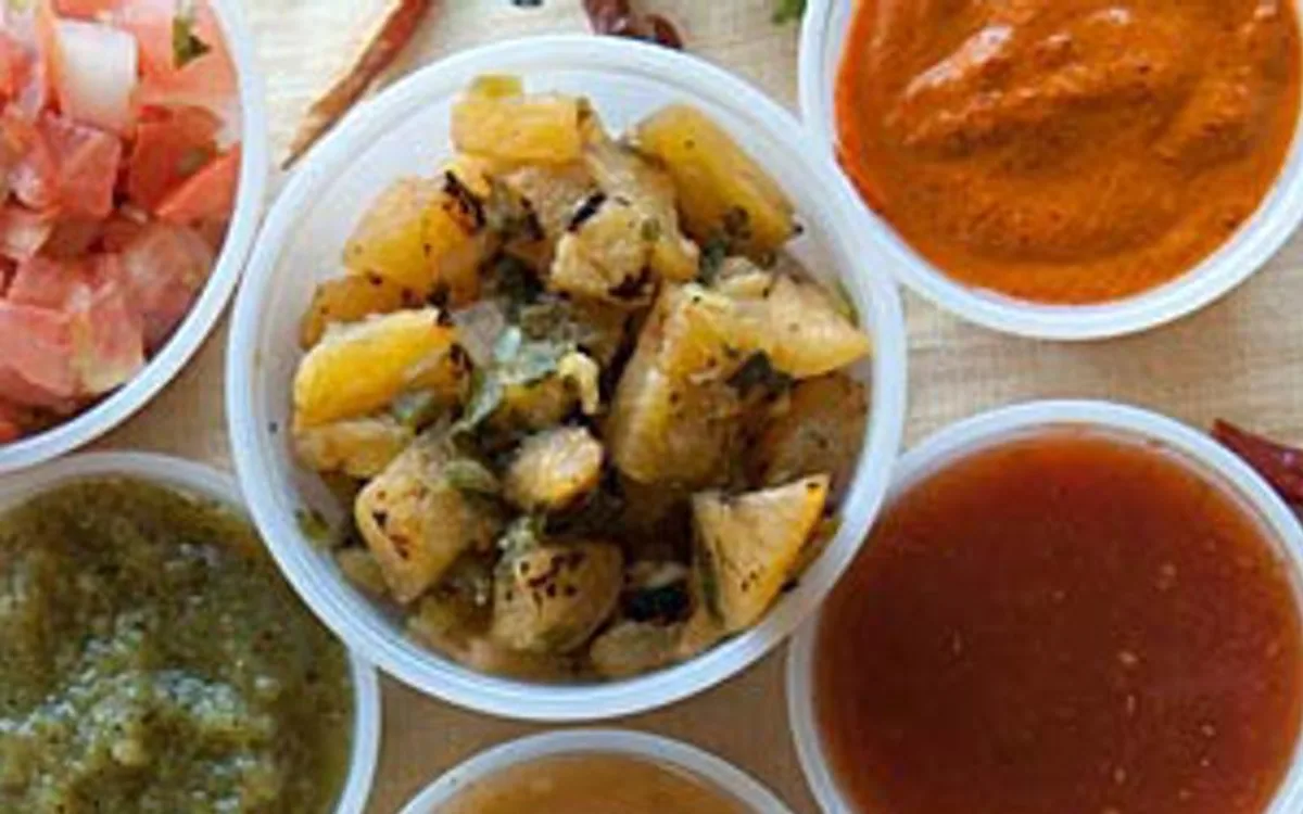 Small bowls of assorted sauces, diced potatoes, and chopped tomatoes on a table.